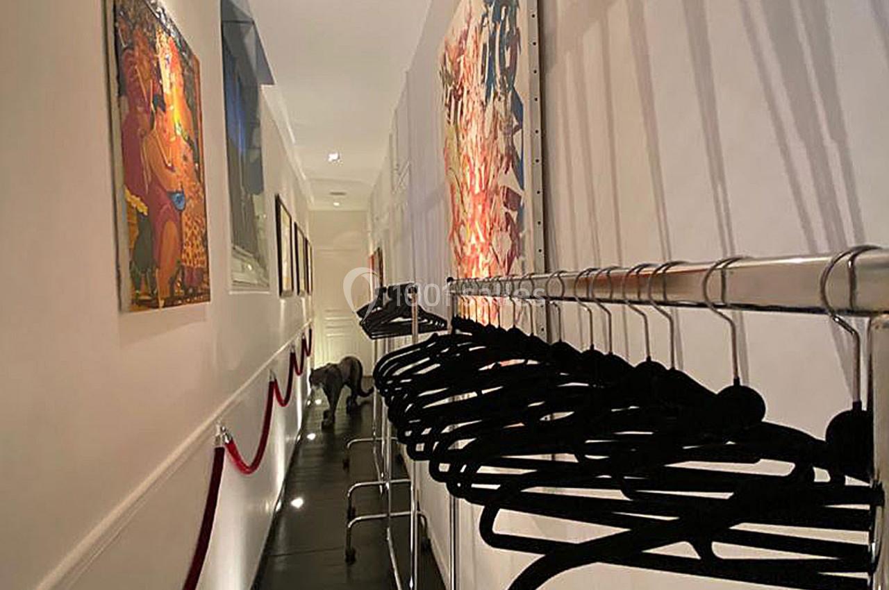 Portant avec des cintres noirs alignés dans un couloir éclairé, décoré de tableaux accrochés aux murs blancs.