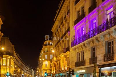 Table ronde en métal noir avec chandelier et chaises, placée sur un balcon avec vue sur une façade d'immeuble haussmannien.
