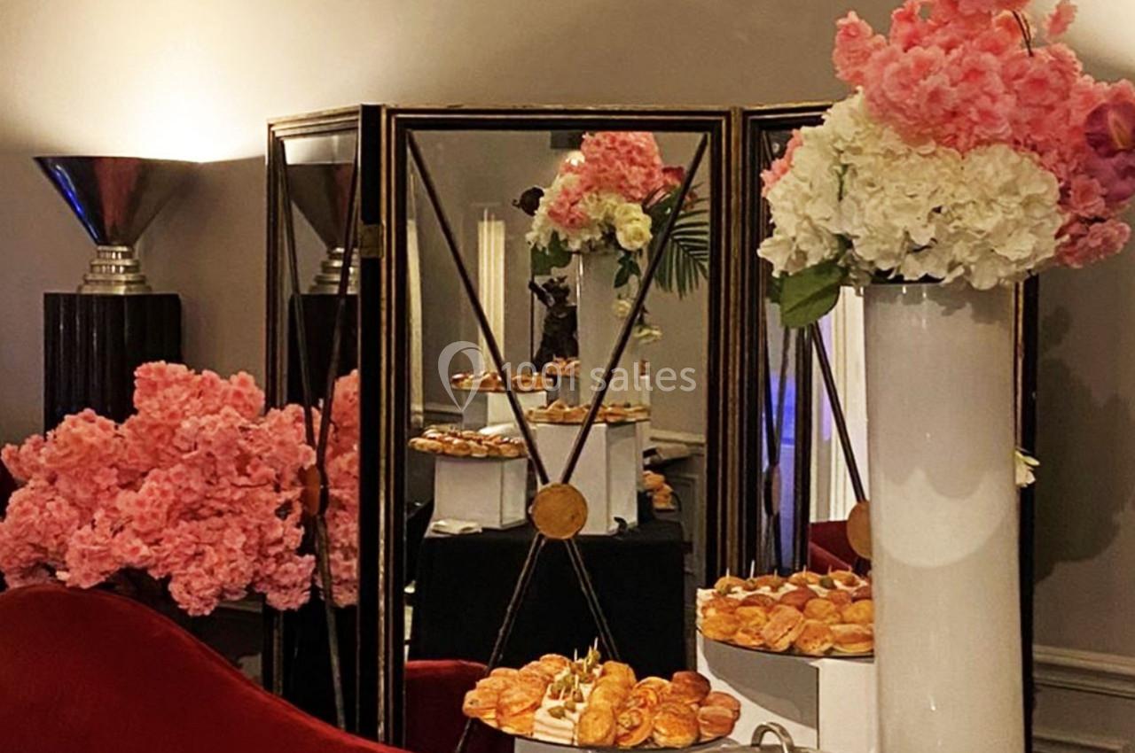 Buffet de viennoiseries disposé devant des miroirs, entouré de fleurs roses et blanches dans un décor élégant.