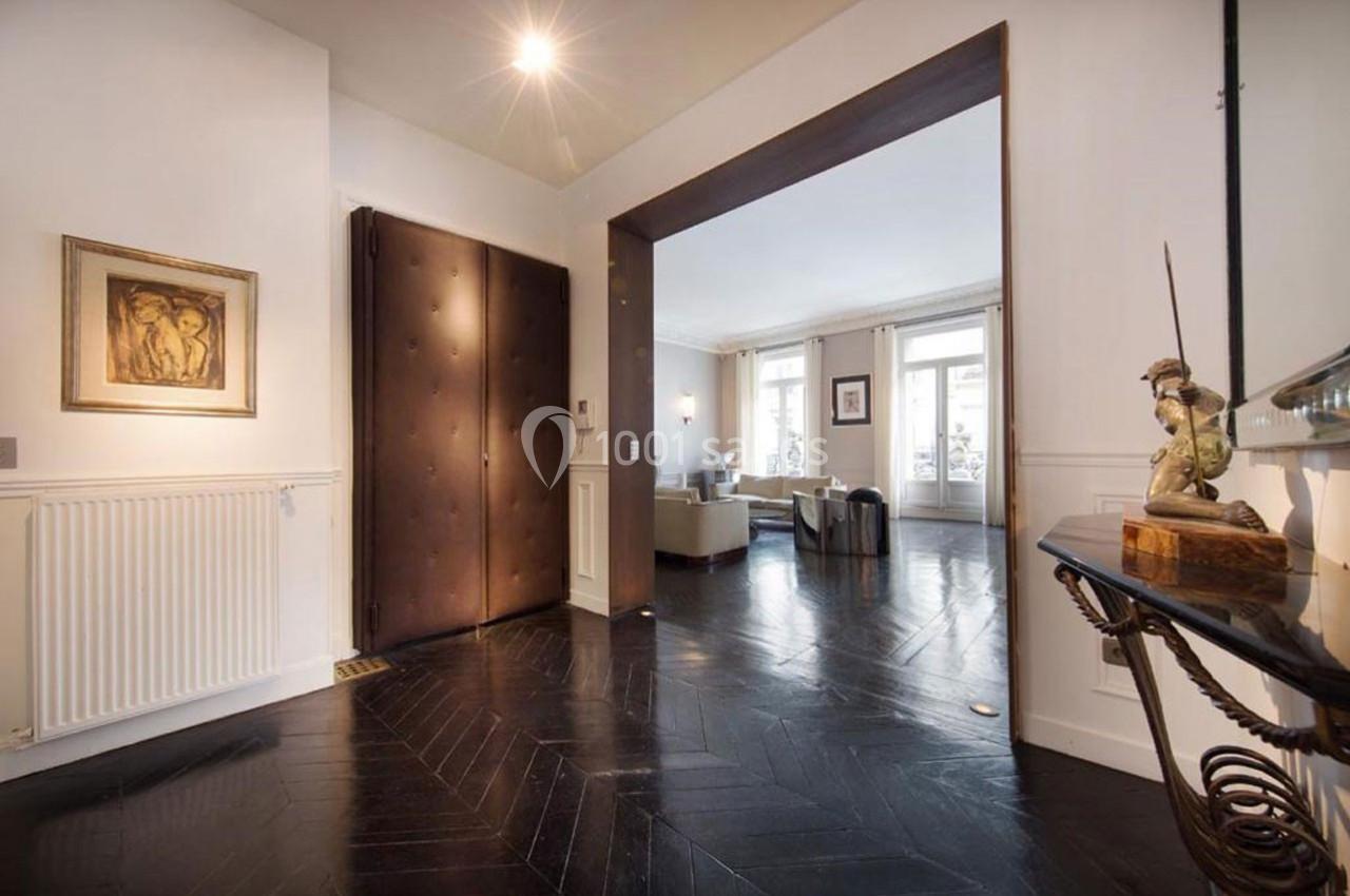 Entrée lumineuse avec parquet sombre, ouvrant sur un salon avec grandes fenêtres et mobilier clair.