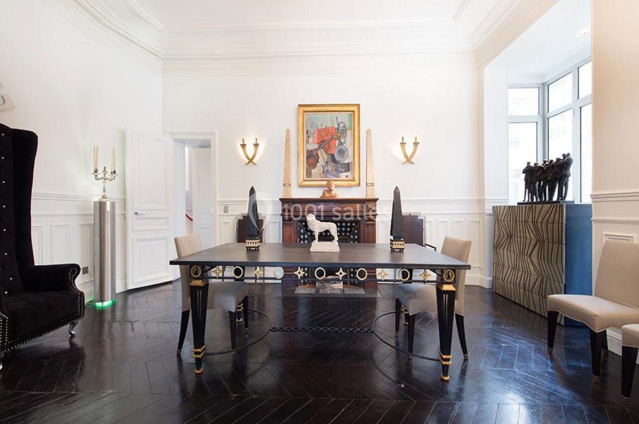 Salle lumineuse avec parquet sombre, table élégante, chaises modernes, cheminée décorée et tableau coloré au mur.