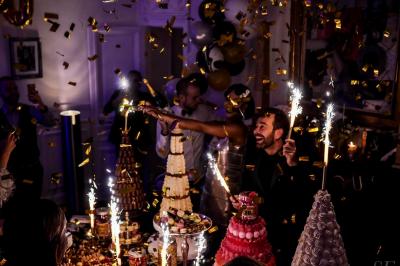 Table ronde en métal noir avec chandelier et chaises, placée sur un balcon avec vue sur une façade d'immeuble haussmannien.