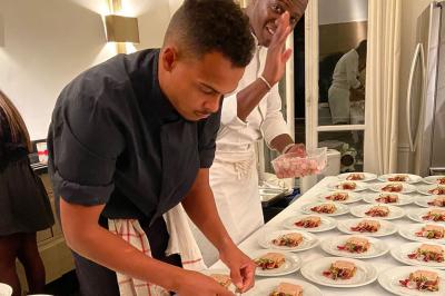 Table ronde en métal noir avec chandelier et chaises, placée sur un balcon avec vue sur une façade d'immeuble haussmannien.
