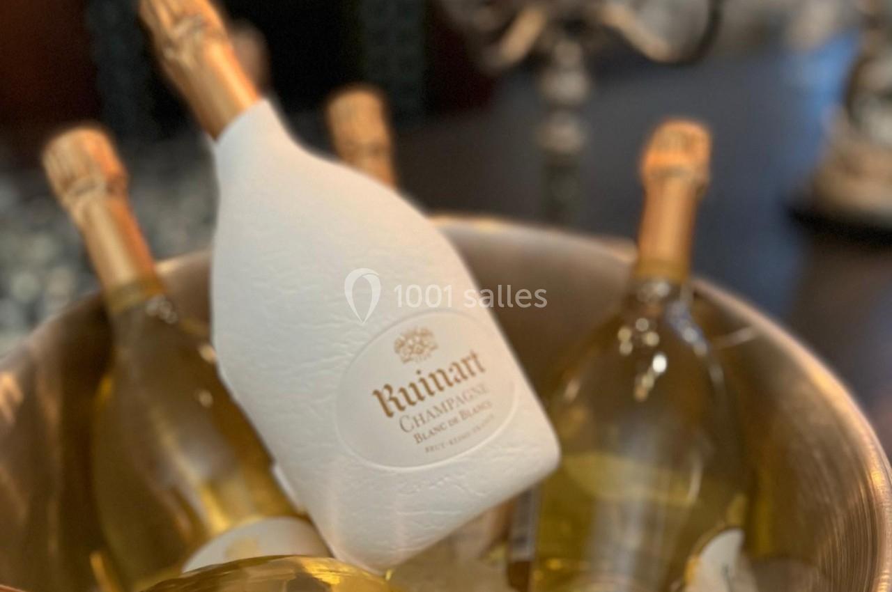 Seau en métal rempli de bouteilles de champagne sur glace, avec des chandeliers en arrière-plan.