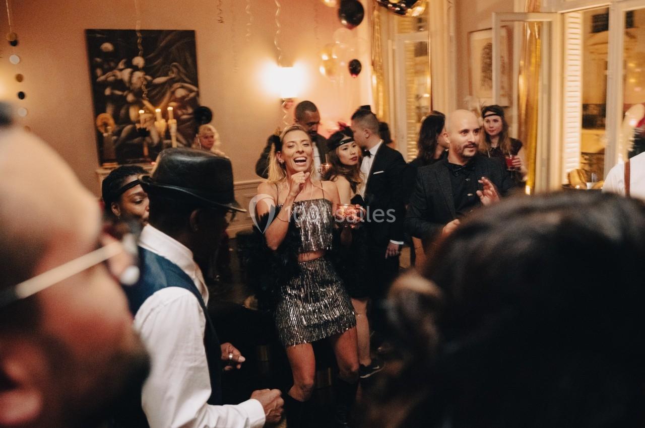 Groupe de personnes dansant et discutant lors d'une fête dans une pièce décorée avec des ballons et des guirlandes.