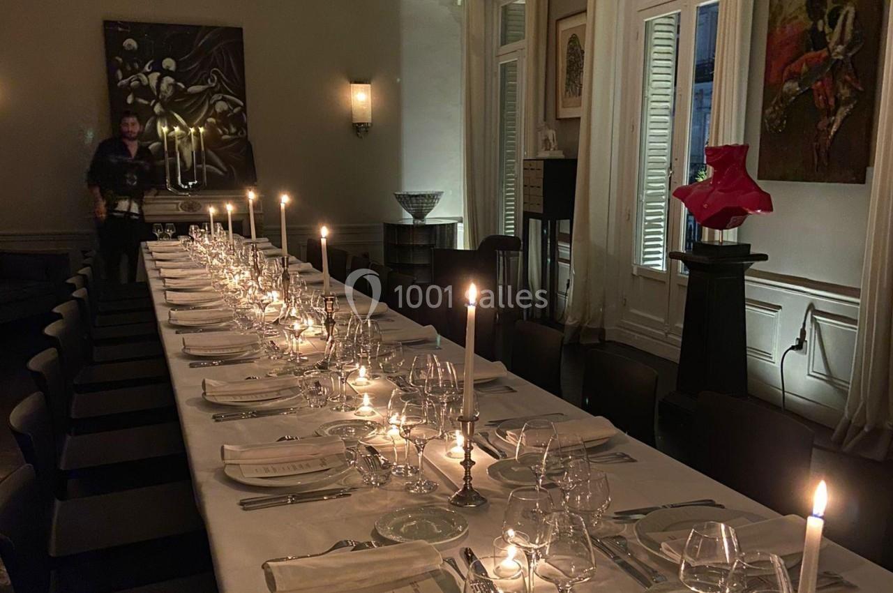 Grande table élégamment dressée avec chandeliers allumés dans une salle à la lumière tamisée.