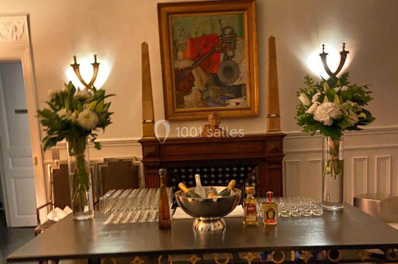 Table dressée avec des verres, une coupe de champagne et des bouteilles, encadrée par deux bouquets de fleurs dans un salon…