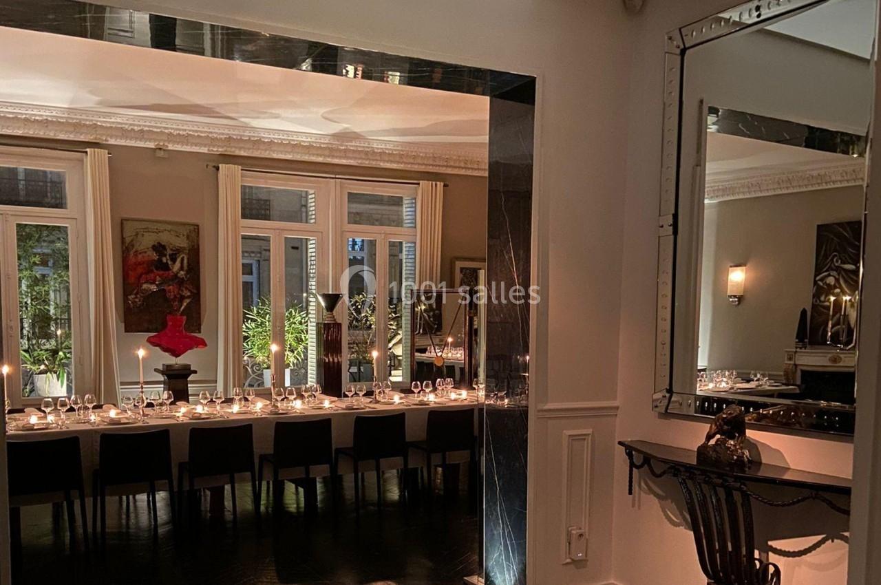 Salle à manger élégante avec une longue table dressée, éclairée par des bougies, et des miroirs reflétant la lumière.