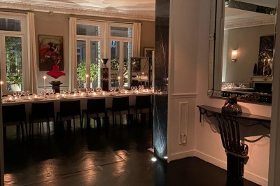 Table ronde en métal noir avec chandelier et chaises, placée sur un balcon avec vue sur une façade d'immeuble haussmannien.