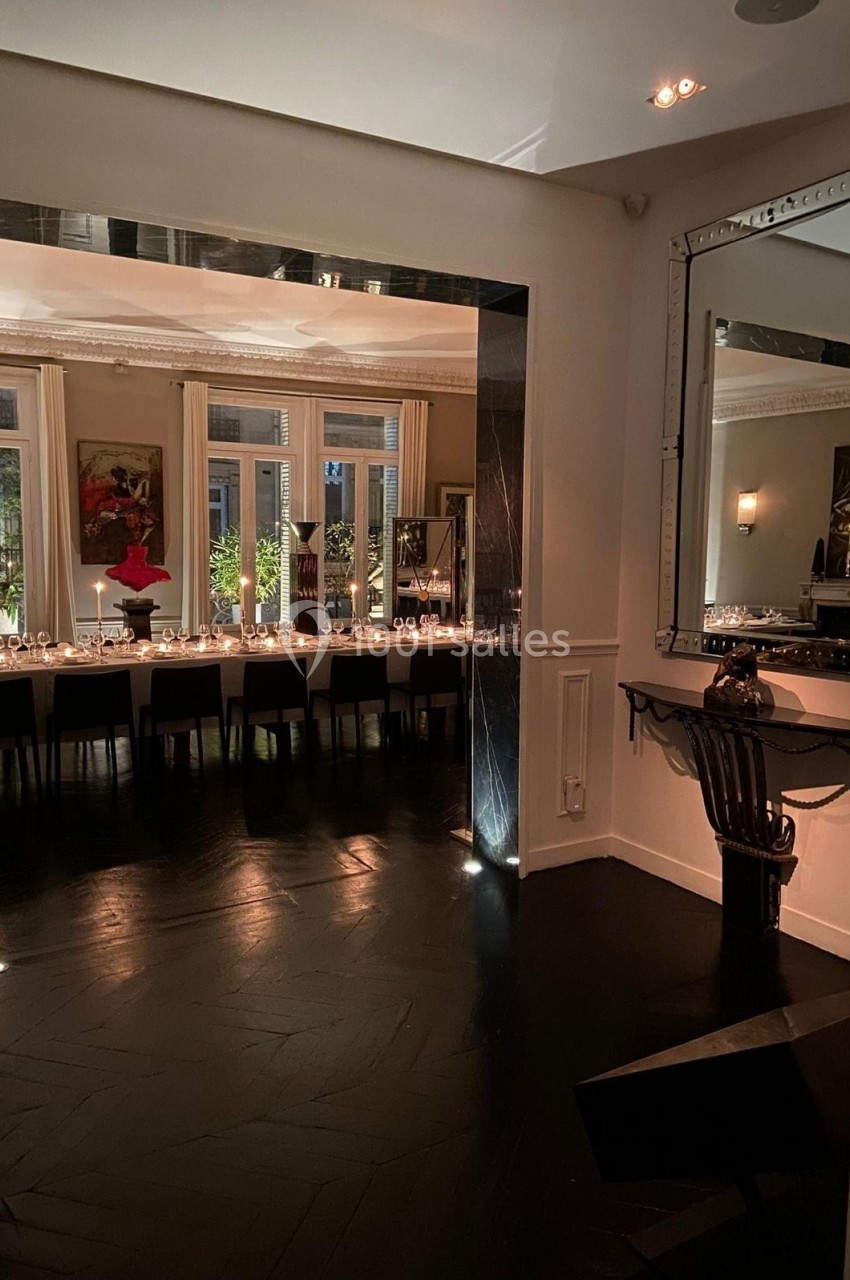 Salle à manger élégante avec une grande table dressée, éclairée par des bougies, et un miroir reflétant la pièce.