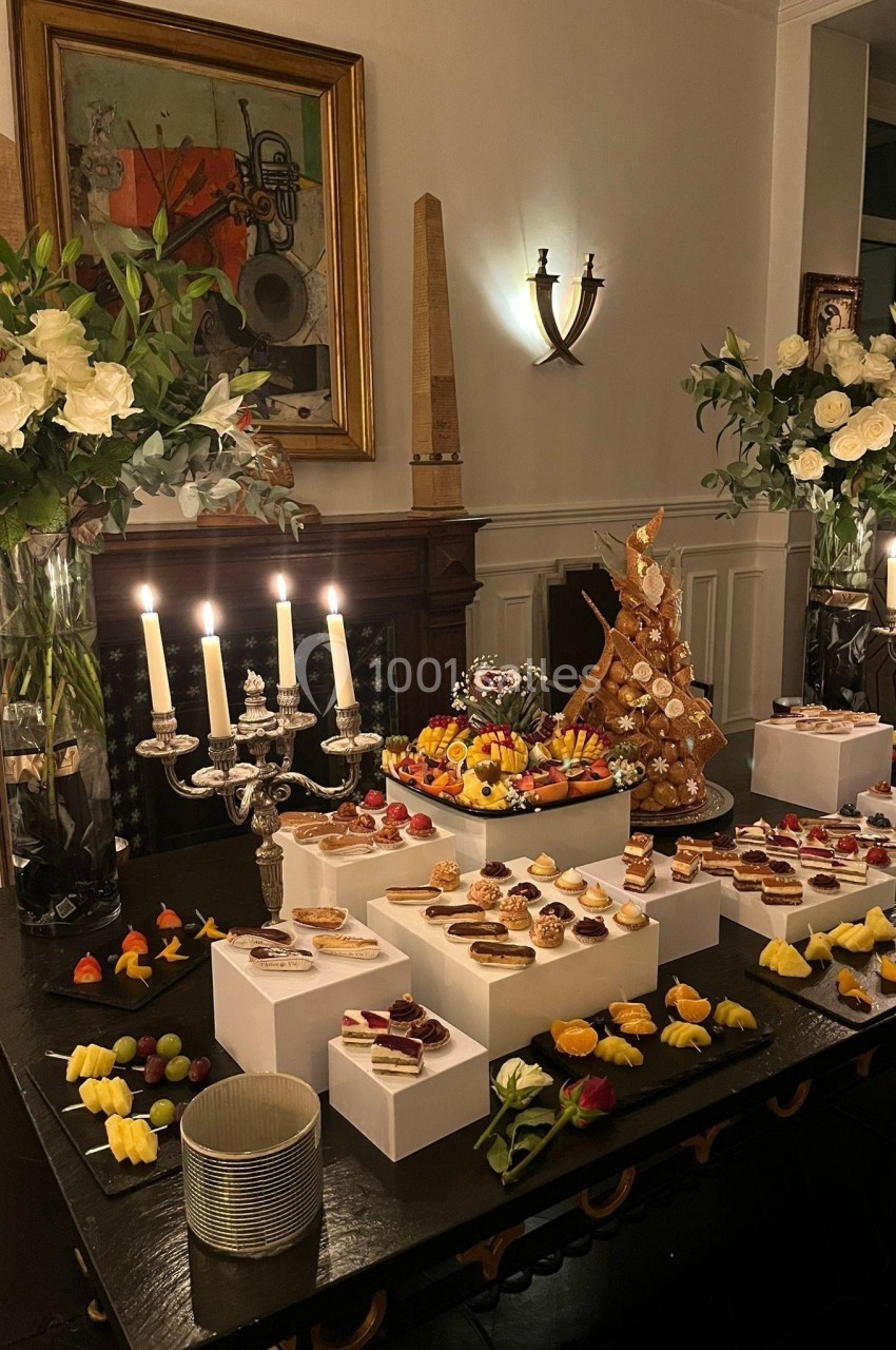 Table garnie de desserts variés, bougies allumées et décorations florales dans une pièce élégante.