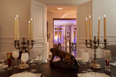 Table ronde en métal noir avec chandelier et chaises, placée sur un balcon avec vue sur une façade d'immeuble haussmannien.