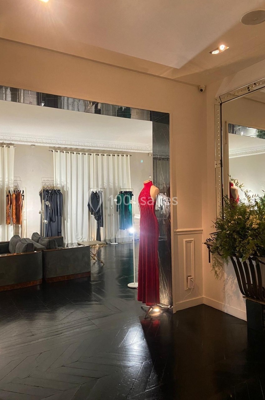 Boutique élégante avec un mannequin portant une robe rouge, des vêtements suspendus et un grand miroir réfléchissant la…