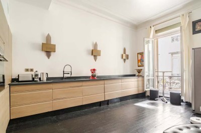 Table ronde en métal noir avec chandelier et chaises, placée sur un balcon avec vue sur une façade d'immeuble haussmannien.