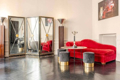 Table ronde en métal noir avec chandelier et chaises, placée sur un balcon avec vue sur une façade d'immeuble haussmannien.