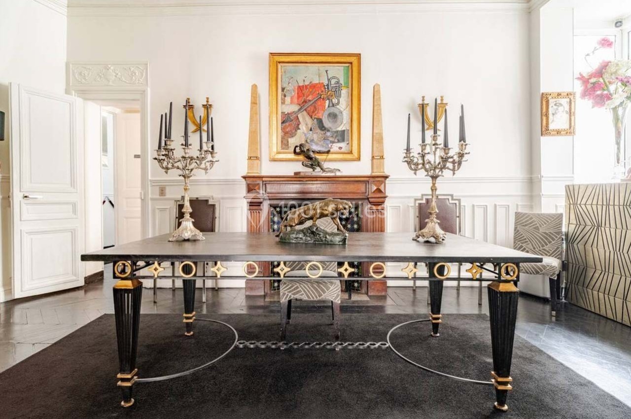 Salle à manger élégante avec table noire ornée, chandeliers, sculpture de panthère et tableau coloré au mur.