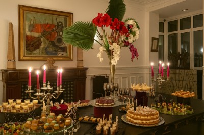 Table garnie de pâtisseries variées, éclairée par des chandeliers, avec des fleurs et une pièce montée en arrière-plan.