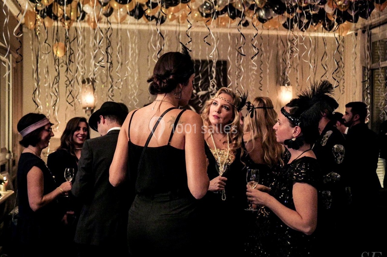 Personnes en tenue de soirée discutant dans une salle décorée de ballons et de guirlandes suspendues.