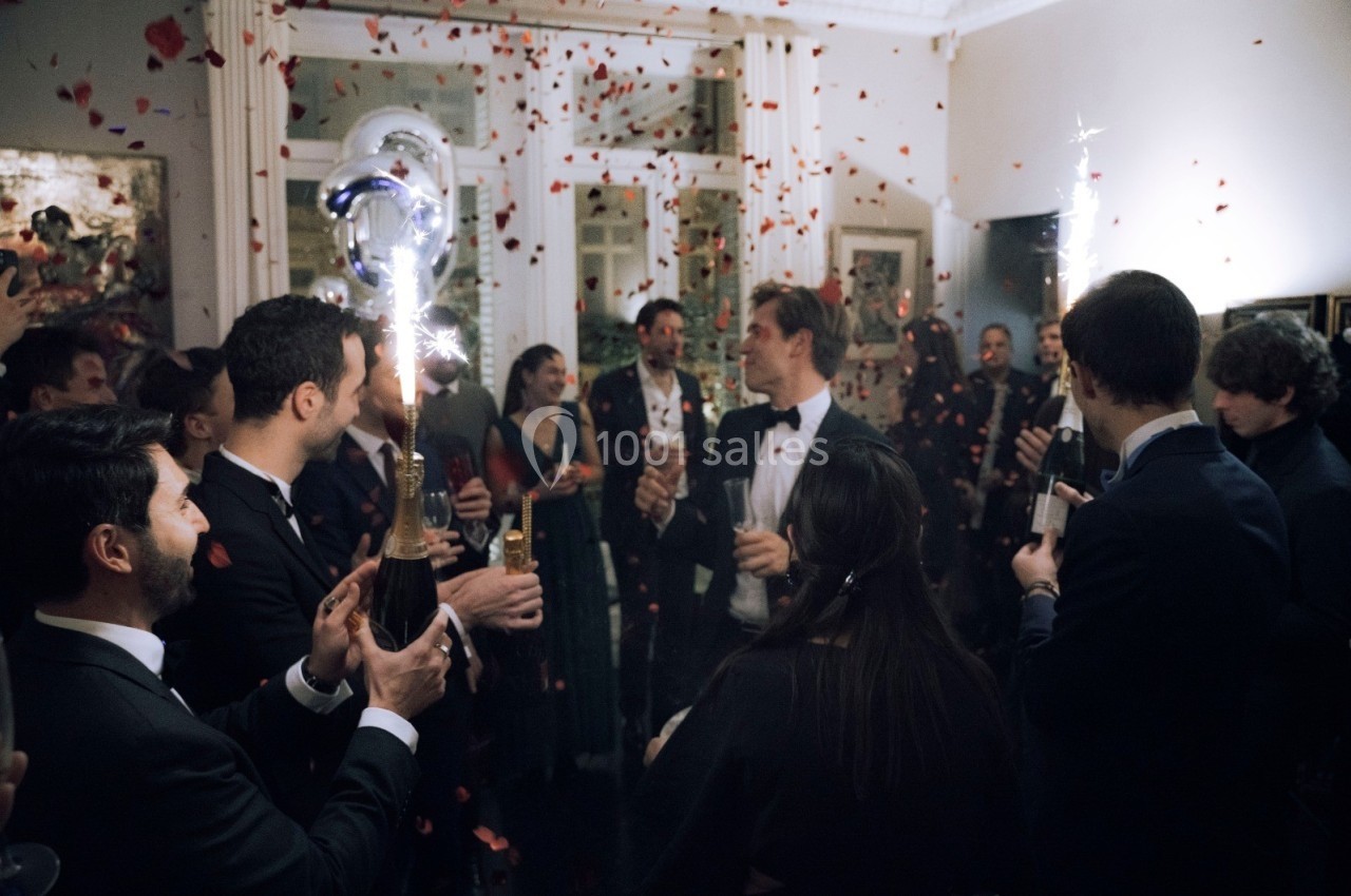 Groupe de personnes en tenue de soirée célébrant avec des bouteilles de champagne et des confettis dans une pièce festive.