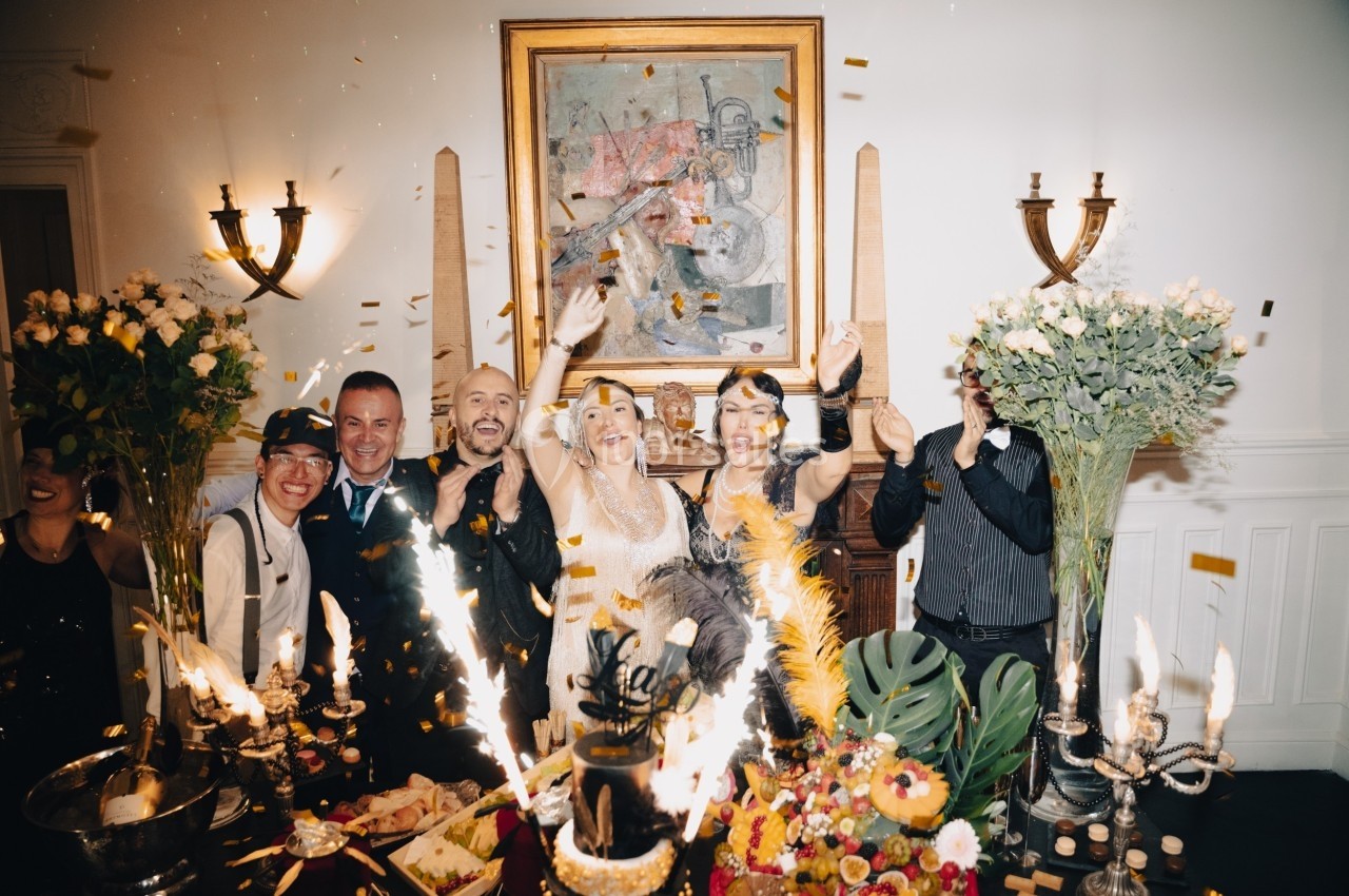 Des personnes célèbrent joyeusement dans une salle décorée, entourées de fleurs, de bougies et de confettis.