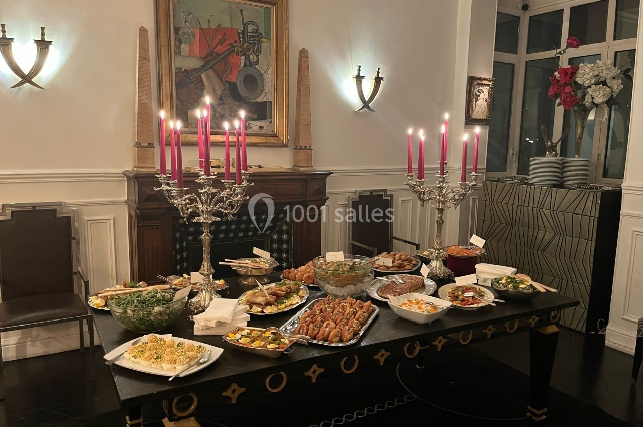 Table dressée avec divers plats et bougeoirs ornés de bougies roses, dans une salle élégante avec cheminée et décorations…