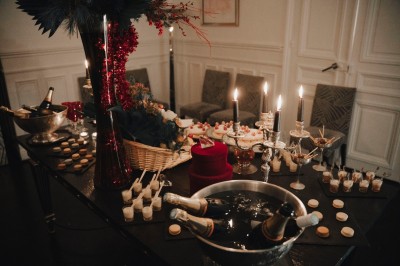 Table garnie de pâtisseries variées, éclairée par des chandeliers, avec des fleurs et une pièce montée en arrière-plan.