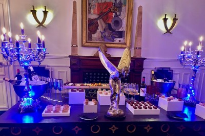 Table garnie de pâtisseries variées, éclairée par des chandeliers, avec des fleurs et une pièce montée en arrière-plan.