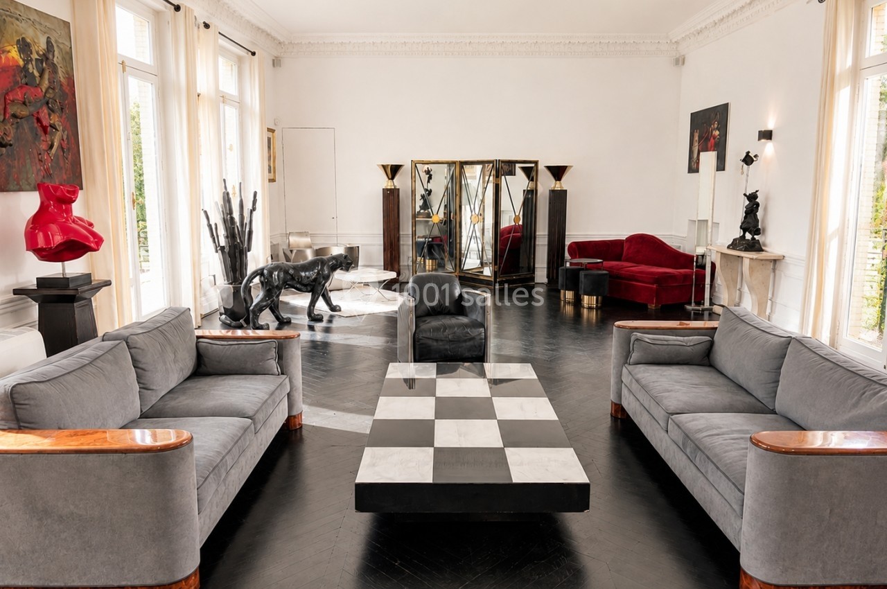Location salle Paris 8 (Paris) - Le Loft Triangle d'Or Champs-Élysées #2 Salon spacieux avec mobilier design, canapé gris, table basse damier, sculptures et miroirs décoratifs.