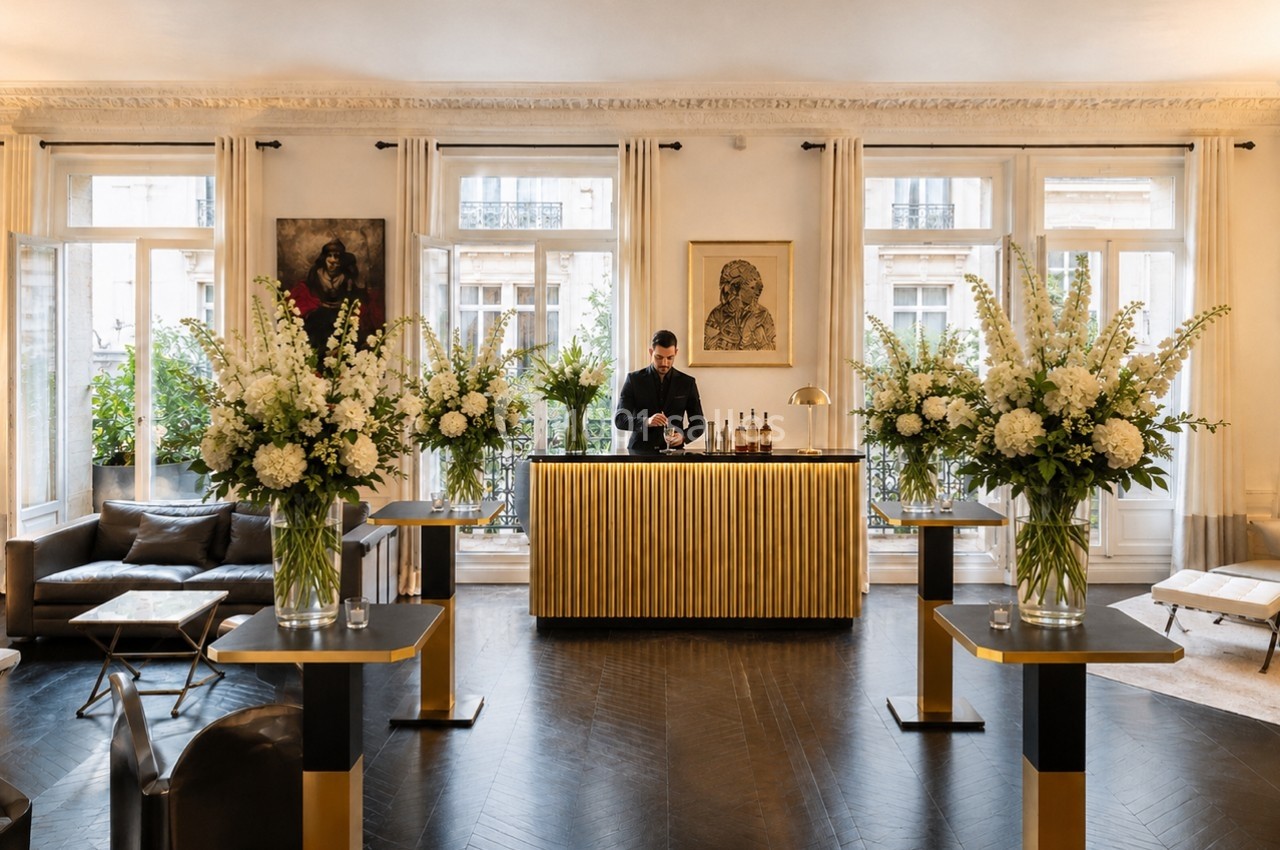Location salle Paris 8 (Paris) - Le Loft Triangle d'Or Champs-Élysées #42 Un barman prépare des boissons derrière un comptoir doré dans un salon élégant décoré de grandes compositions florales.