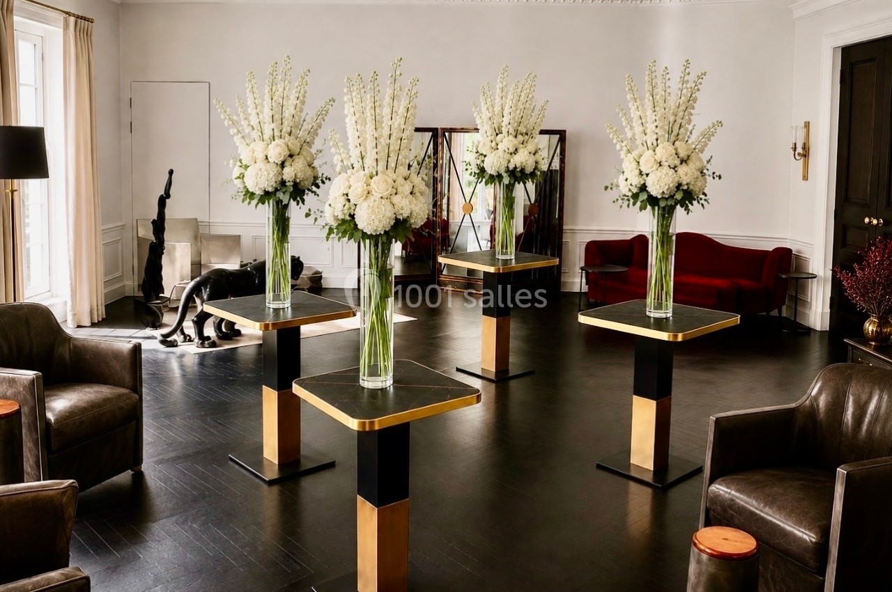 Location salle Paris 8 (Paris) - Le Loft Triangle d'Or Champs-Élysées #4 Salle élégante avec quatre compositions florales blanches sur des tables modernes, entourées de fauteuils et d'un canapé…