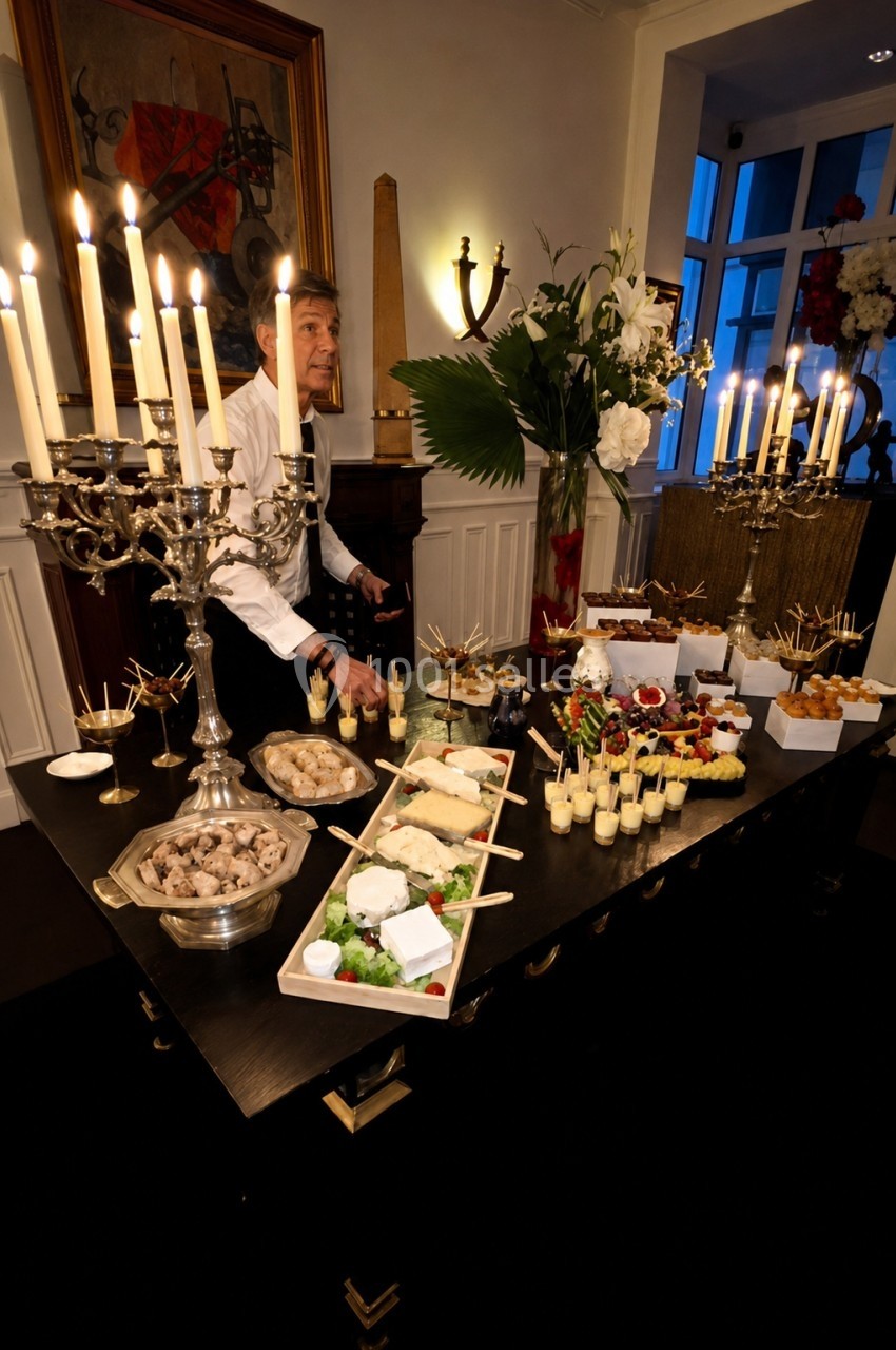 Location salle Paris 8 (Paris) - Le Loft Triangle d'Or Champs-Élysées #54 Table de buffet élégante avec chandeliers, plats variés et serveur en arrière-plan dans une salle éclairée.