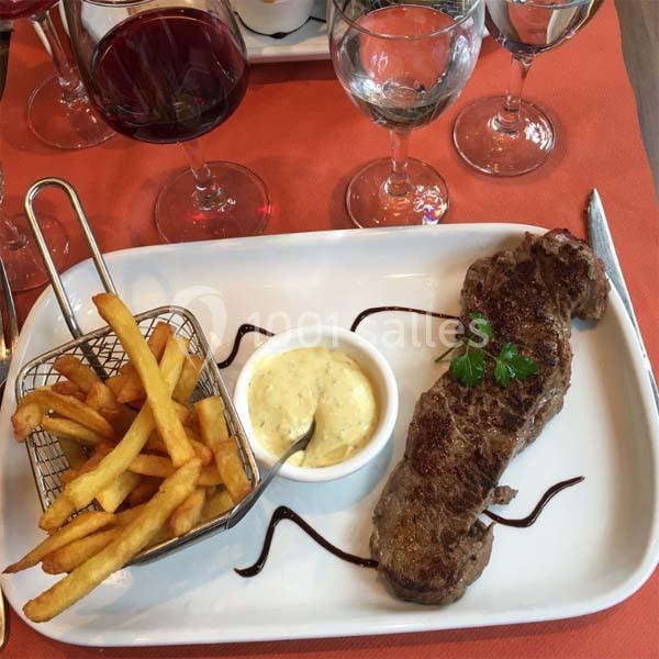 Assiette avec un steak grillé, des frites dans une petite panière, une sauce et des décorations en filet de vinaigre…