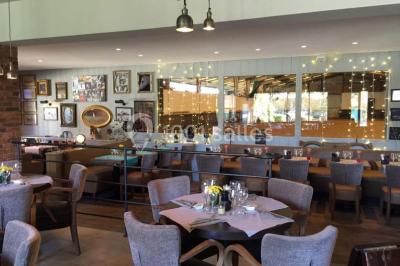 Salle de restaurant lumineuse avec table dressée, grandes fenêtres donnant sur un jardin et murs en briques.