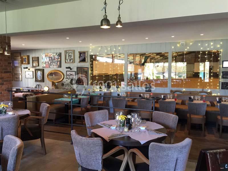 Salle de restaurant lumineuse avec tables dressées, chaises rembourrées et décorations murales variées.