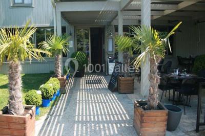 Salle de restaurant lumineuse avec table dressée, grandes fenêtres donnant sur un jardin et murs en briques.