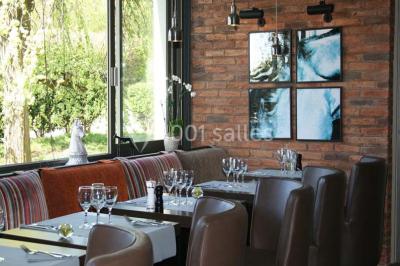 Salle de restaurant lumineuse avec table dressée, grandes fenêtres donnant sur un jardin et murs en briques.