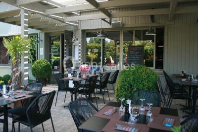 Salle de restaurant lumineuse avec table dressée, grandes fenêtres donnant sur un jardin et murs en briques.