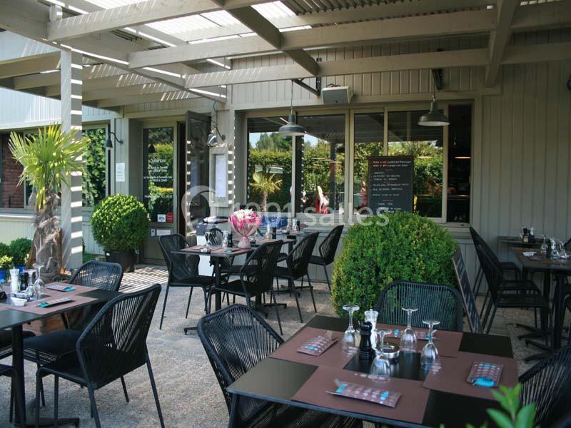 Terrasse d'un restaurant avec tables dressées, chaises noires, plantes décoratives et menu affiché sur un tableau noir.