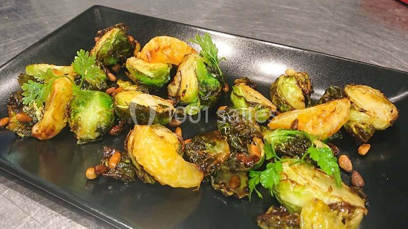 Choux de Bruxelles rôtis avec pignons de pin et herbes fraîches, présentés sur une assiette noire.