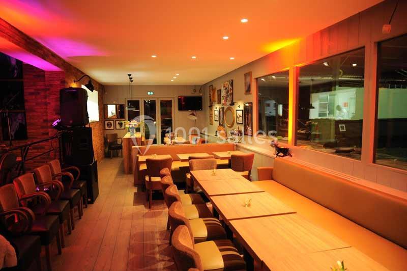 Salle de restaurant chaleureuse avec éclairage tamisé, tables en bois, chaises rembourrées et décorations murales.