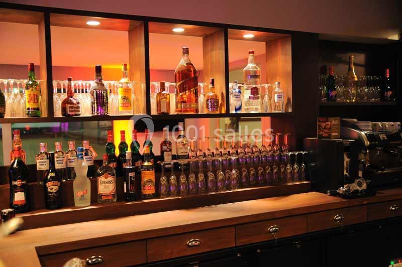 Étagères éclairées avec une variété de bouteilles d'alcool et un comptoir en bois dans un bar.