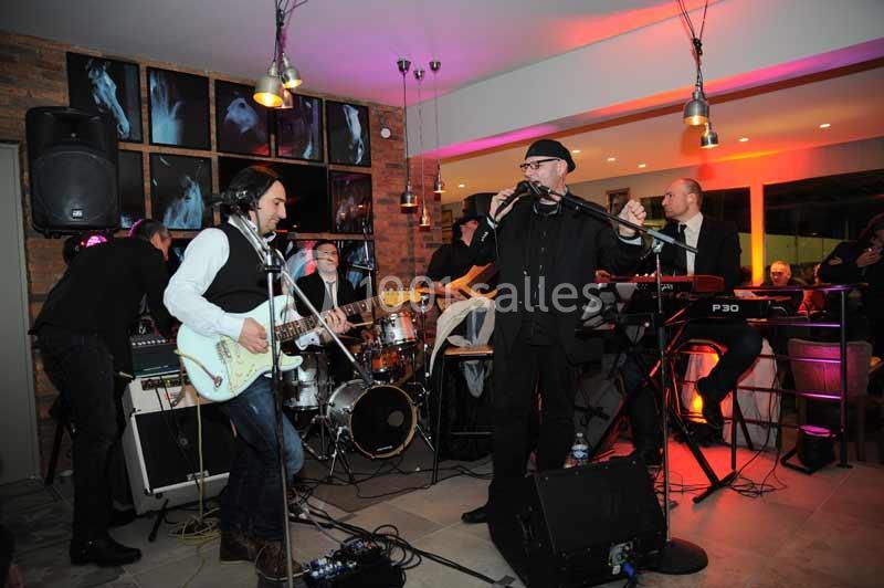 Un groupe de musiciens joue en live dans un espace intérieur, avec guitares, batterie et clavier.