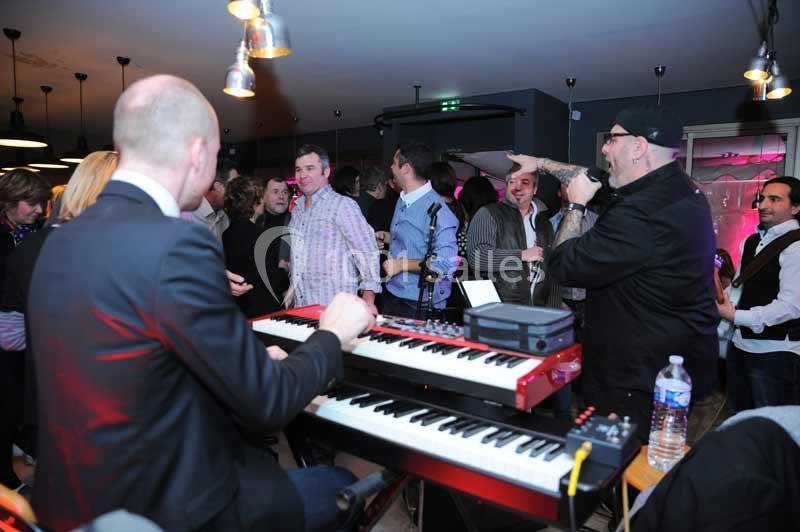 Un groupe de personnes dans un bar, avec un musicien jouant du clavier et un chanteur s'adressant au public.