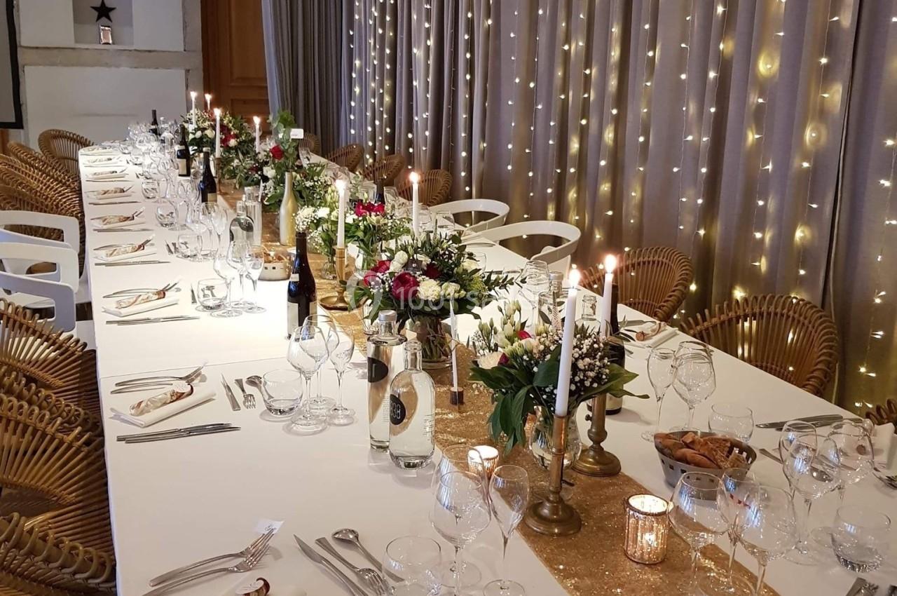 Table élégamment dressée pour un dîner, décorée de bougies, fleurs et guirlandes lumineuses en arrière-plan.