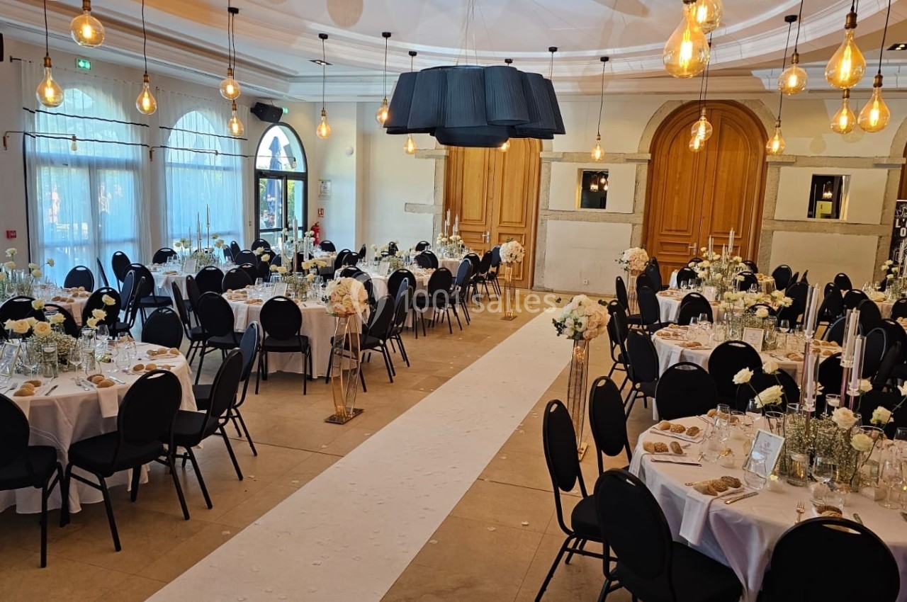 Salle de réception élégamment décorée avec des tables rondes, des chaises noires et des arrangements floraux blancs.
