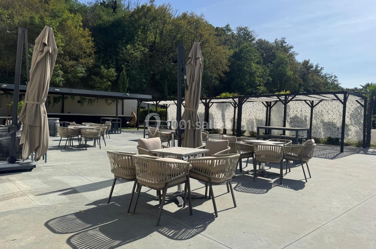 Terrasse extérieure avec tables et chaises en rotin, parasols fermés, entourée de verdure et d'un mur végétalisé.
