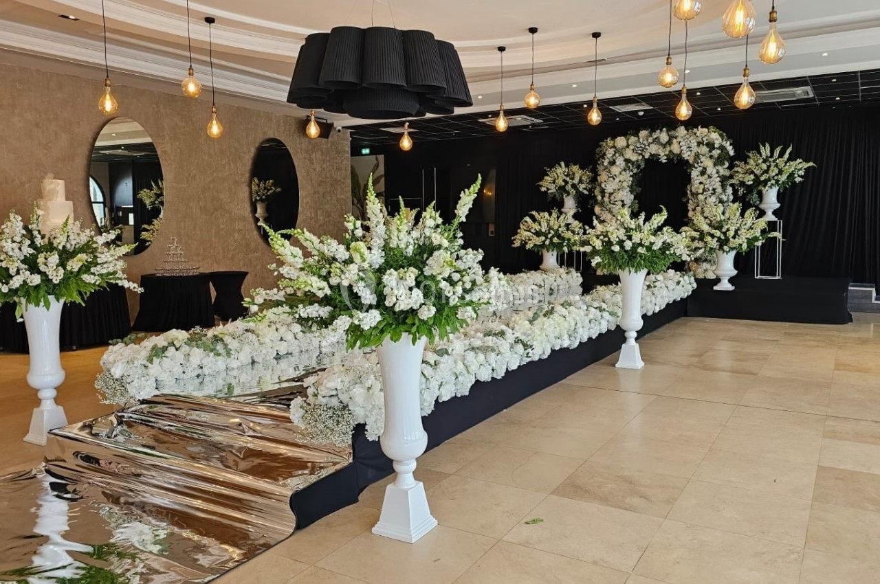 Salle décorée pour un événement avec des fleurs blanches, un tapis argenté et un éclairage suspendu.