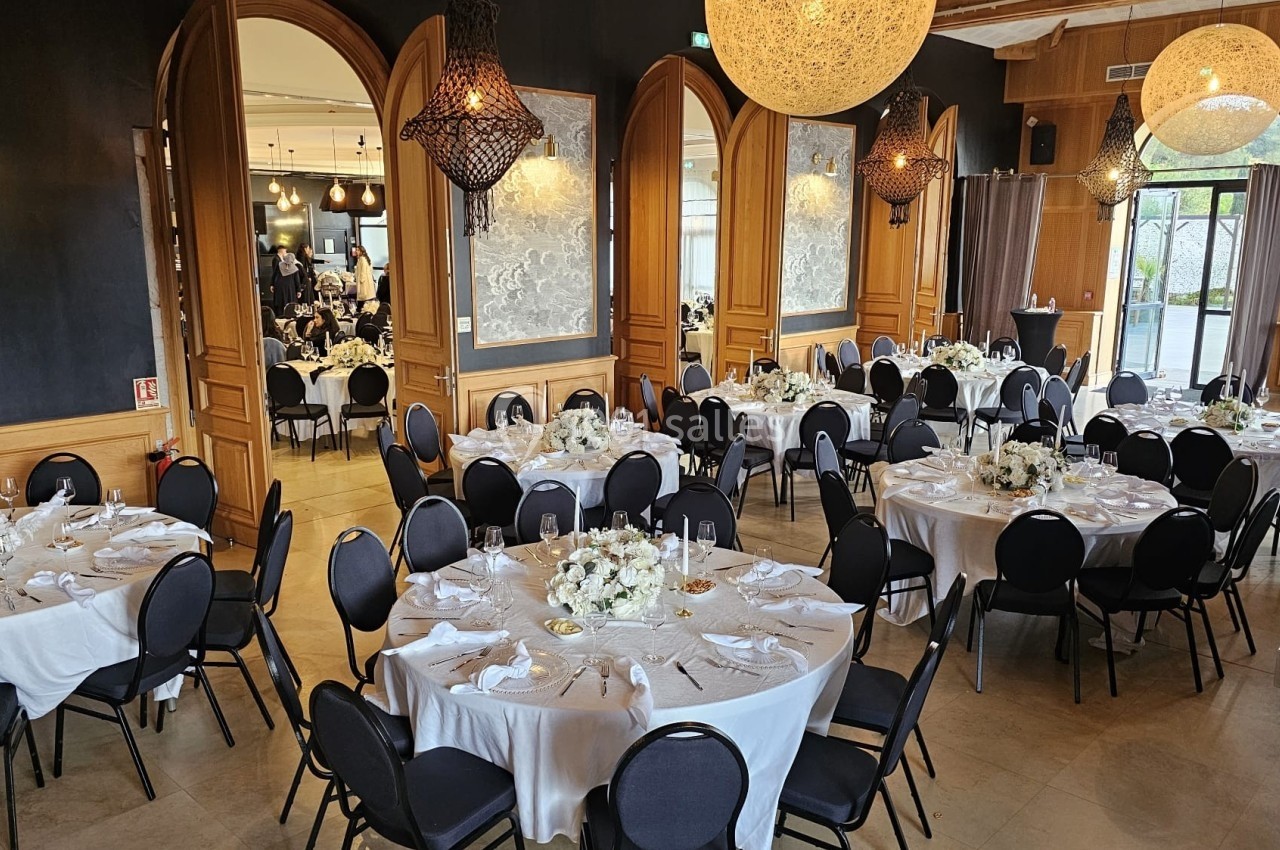 Salle de réception élégante avec tables rondes dressées de nappes blanches et décorations florales.
