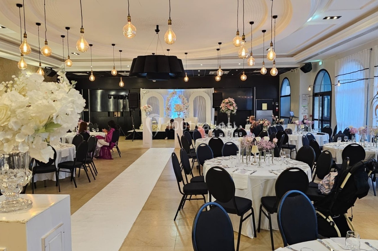 Salle de réception élégante avec tables dressées, décor floral et éclairage suspendu dans une ambiance lumineuse.