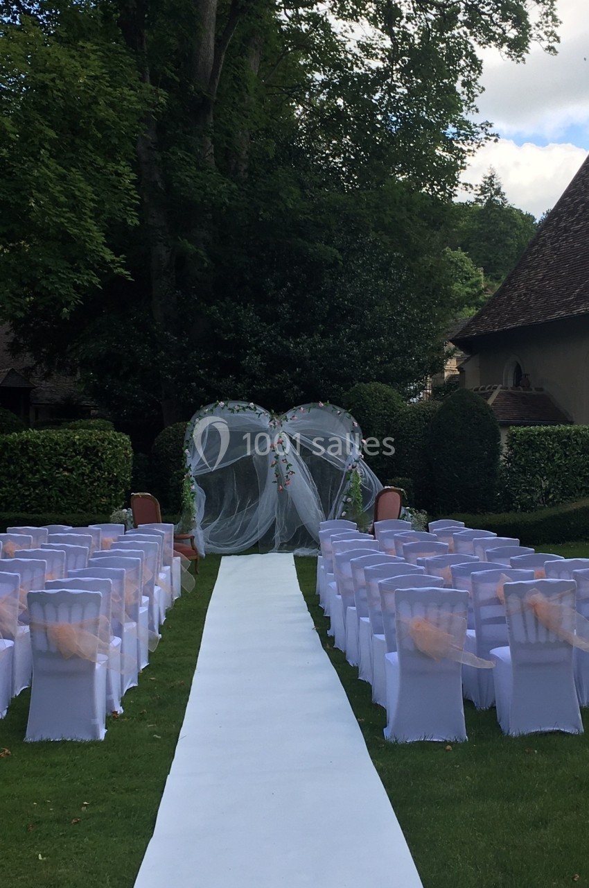 Allée centrale bordée de chaises blanches menant à une arche décorée pour une cérémonie en plein air dans un jardin.